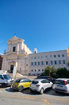 Civitavecchia, Italy - December 19, 2024: A historic church facade contrasts with modern buildings and urban life, captured on a sunny day. Concept: Architecture, history, urban contrast.