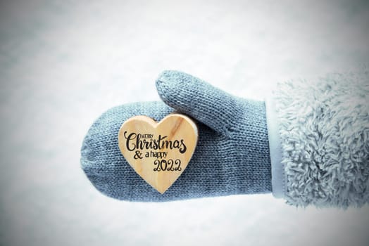 Heart With English Calligraphy Merry Christmas And A Happy 2022. Human Hand In A Glove With Fleece And Snow.