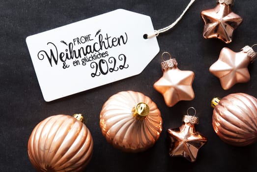 One Label With German Calligraphy Frohe Weihnachten Und Ein Glueckliches 2022 Means Merry Christmas And A Happy 2022. Golden Christmas Ball Ornament On Black Background.