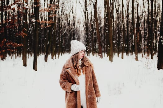 Photo of young beautiful woman in fur coat standing on the white snow in winter forest. Girl is smiling and happy with closed eyes. Female has winter vacation, happily waiting for Christmas holidays