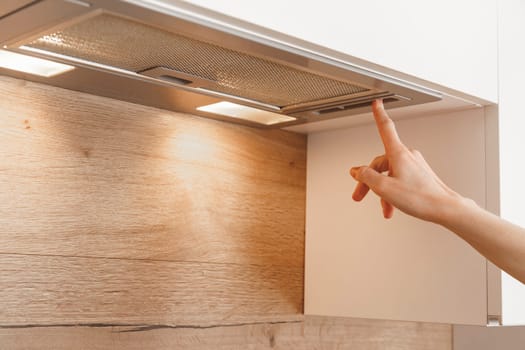 Woman hand turn on embedded cooker hood in white modern kitchen