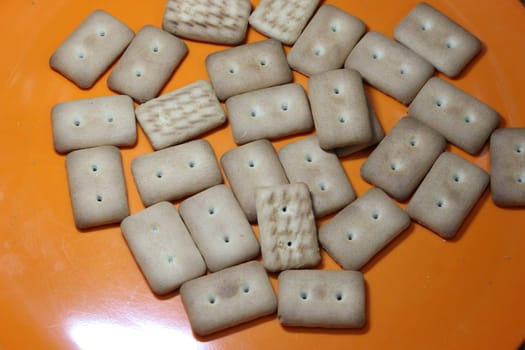 Close up top view of of biscuit cookies. Many rectangular biscuits with small pores in red plate