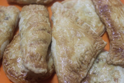 Closeup of delicious home made spicy and crunchy samosa pastries placed in a white ceramic plate on wooden floor