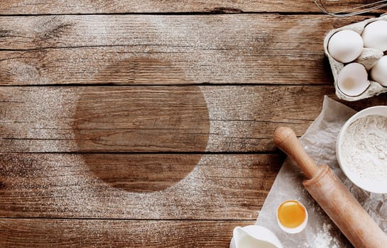 Christmas baking ingredients, kitchen utensils on old wooden background. Cooking dough, preparing egg yolk, flour, rolling pin, parchment paper, whisk, salt. Concept flat lay photo with copy space