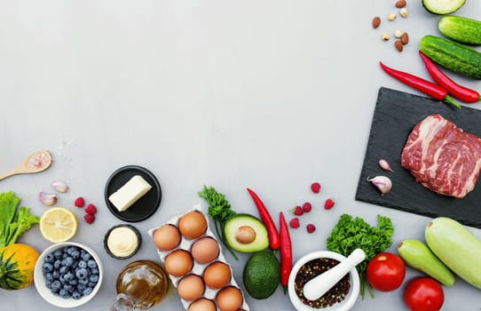 Flat lay with different food, rib-eye or sirloin beef meat steak, organic vegetables, bio fruits, berries, nuts, spices, herbs, olive oil, eggs. Copy space area for some text. Gray concrete background