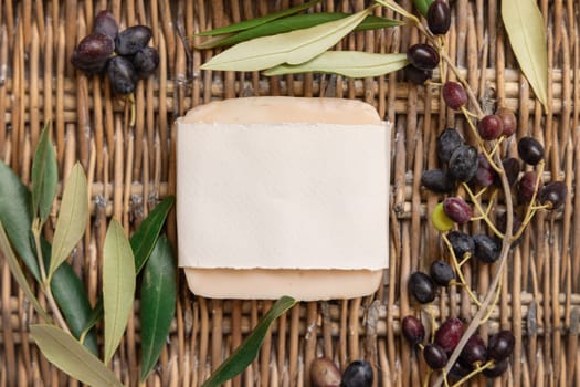 Handmade Soap bar laying on a wooden wattled table with paper wrapping package with olive branches, top view. Soap mockup Mediterranean flat lay, Healthy lifestyle concept