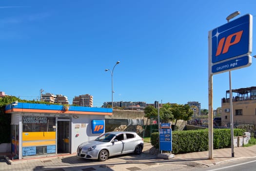Civitavecchia, Italia - December 27, 2024: A fuel station with a modern car and clear signage, framed by an urban skyline under a bright blue sky. Concept: City life and transportation essentials.