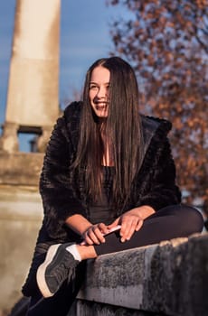 Portrait of Smiling teen girl sitting on the low wall with her legs crossed