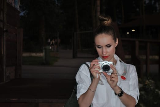 portrait of the young woman taking pictures on a white camera in the evening