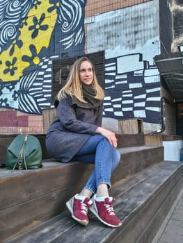 A young woman sits on a wooden staircase near a building in a bohemian quarter in the autumn