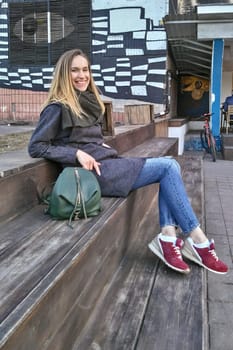 A young woman sits on a wooden step and smiles looking into the camera