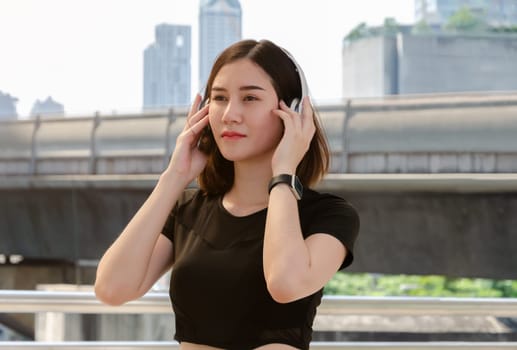 Young fitness woman listening to music on her headphones in urban background and relaxing after exercise. Healthy lifestyle concept.