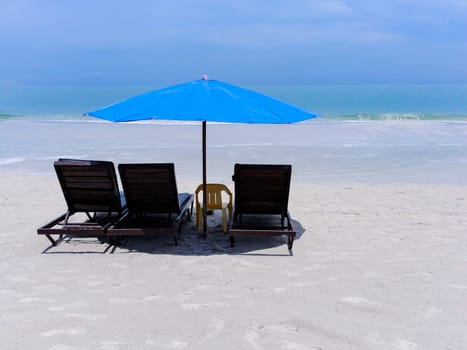 Three sunbeds and a blue umbrella on the beach with white sand on the beach, copy space