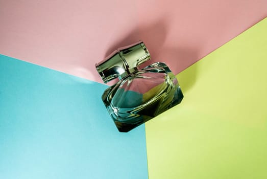 Bottle of perfume on the background of yellow, pink and blue. Top view. Copy space