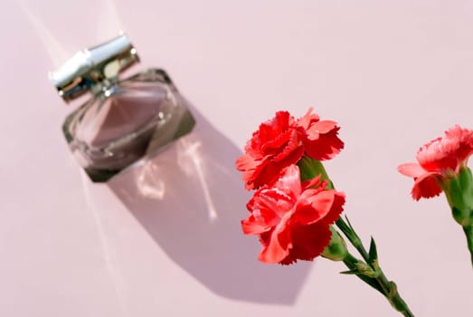 Perfume bottle and carnation flower on a pink background. Copy space