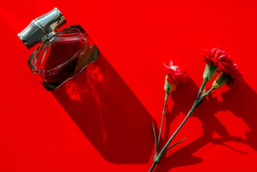 Red carnation flower, perfume bottle on a red background with hard shadows. Copy space