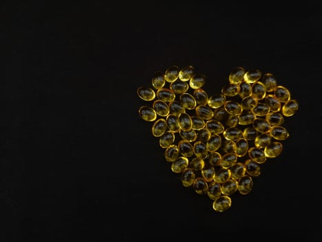 A handful of yellow transparent capsules on a black heart-shaped background, copy space for your text, view from above