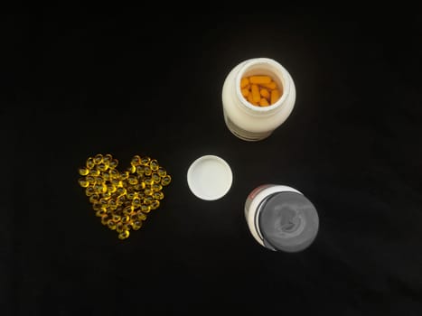 Yellow transparent heart-shaped capsules and jars of pills on a black background