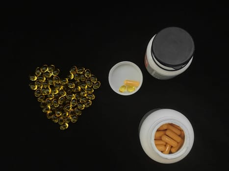 Two jars of medicine, a handful of yellow transparent heart-shaped capsules on a black background