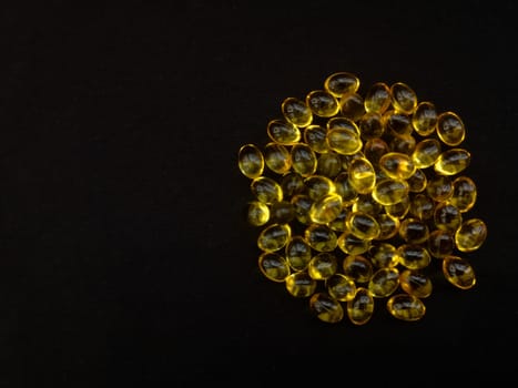 A handful of yellow transparent capsules on a black background in the shape of a circle, copy the space, view from above