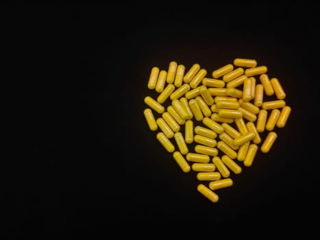 A handful of yellow heart-shaped capsules on a black background, copy space for your text