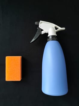 cleaning. Orange sponge and blue sprayer on a black background.