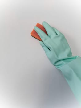 Cleaning and disinfection. A woman in a blue glove holds an orange sponge and washes a light wall.