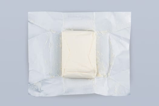top view closeup of opened fresh piece of butter in silver foil protective packaging on grey background