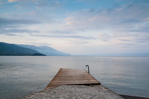 front view landscape of empty wooden swimming dock pier on lake Ohrid with beautiful coastal mountain panorama in the background