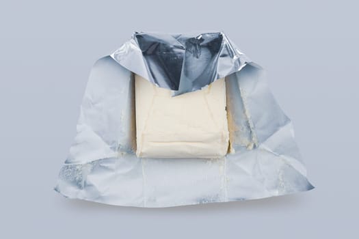 top view closeup of opened fresh piece of butter in silver foil protective packaging on grey background