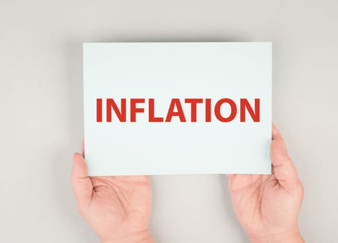 The word inflation is standing on a paper, increasing living costs, hands hold message