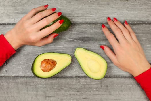 Table top view - woman hands, and avocado cut in half on gray wood desk.