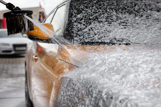 Water and shampoo stream falling on car covered with thick foam, when washed in carwash.