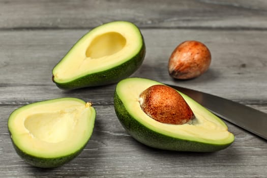 Avocado, cut in half, two seeds and chefs knife on gray wood desk.