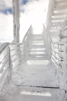 Stairs and rail, completely covered with ice crystals, strong sun back light in background. Freezing winter.