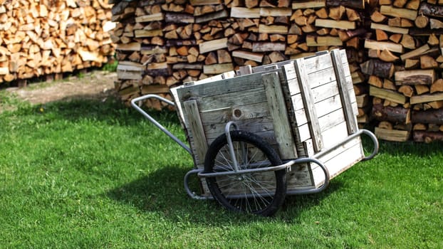 Wood and steel cart with rubber tires, on a green lawn, with piles of stacked chopped firewood in background.