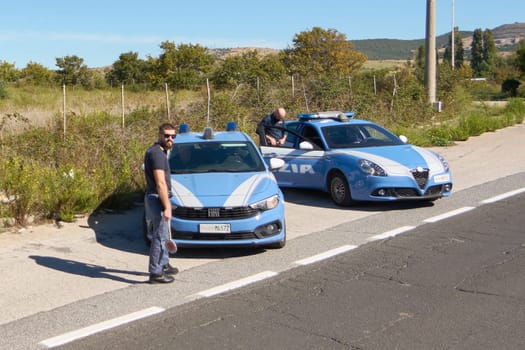 Civitavecchia, Italy - December 27, 2024: Italian police cars, a Fiat and an Alfa Romeo, parked on the road. Officers are present. Concept: police presence and law enforcement in rural areas.