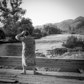 31st of July, Russia, Altay, rural scene with woman on the bridge looking on horison on the mountains background