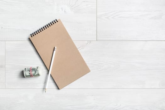 Notepad, pencil and money on wooden background. Flat lay.