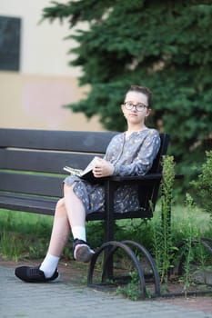 Pensive girl sits on a bench with book in her hands. Selective focus.