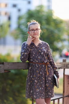 Teenage girl with a book in her hands stands at the fence. Selective focus.