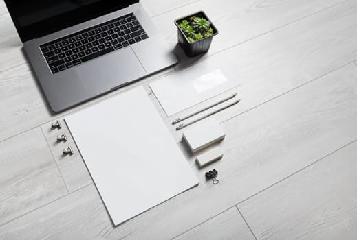 Photo of blank stationery set and laptop on wooden background.