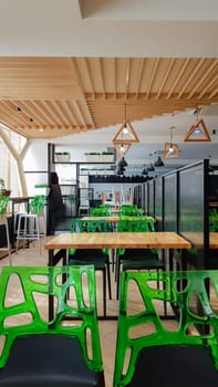 Cafeteria, no people dining room with wooden tables and green chairs. Interior with wood and metal elements. Modern dining areas with window lighting. Ukraine, Kiev - February 19, 2021.