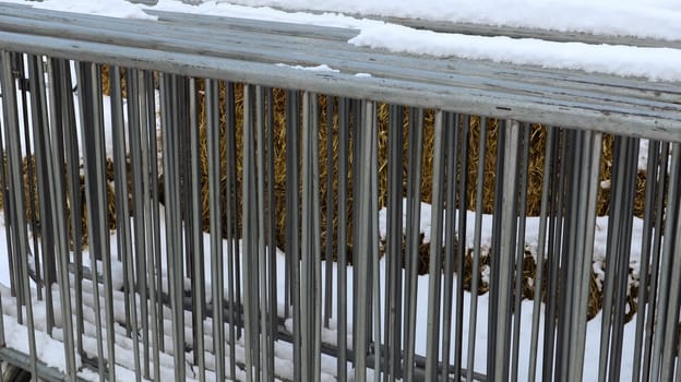 A portable metal event fence is kept in one place at the fair in the snow outdoors in winter. Gray grates for cluttering the area and organizing the queue for the event