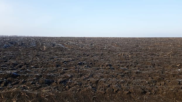 Agricultural field plowed by tractors under blue sky. The field has been plowed, crops have been sown. Close up of soil texture. Rural scene. Farming and food industry. Arable land of chernozem