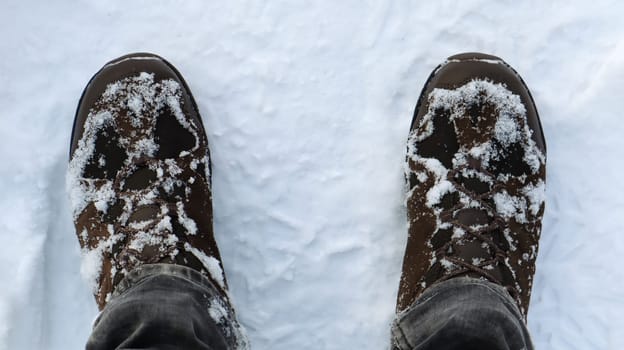 Male legs in snow-covered winter boots, top view. Winter walk in the snow. Focus on your legs. Beautiful white winter weather with fresh snowfall