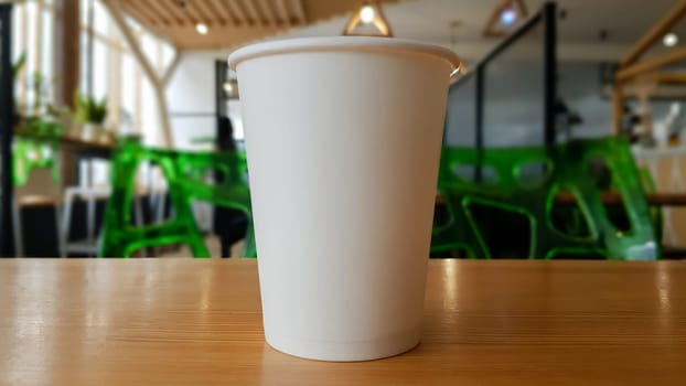 Paper white coffee cup disposable to take or go, on the wooden table of the coffee shop or dining room, place for a designer layout. Hot coffee cup in a cafe