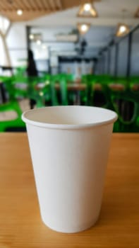 Paper white coffee cup disposable to take or go, on the wooden table of the coffee shop or dining room, place for a designer layout. Hot coffee cup in a cafe