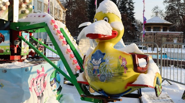 The empty carousel is covered with snow. Close up of snow covered colorful ducks carousel at fun fair carnival during winter daytime