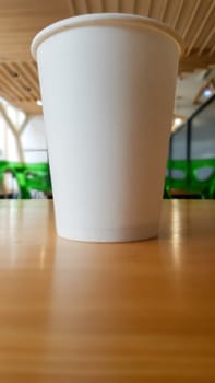Paper white coffee cup disposable to take or go, on the wooden table of the coffee shop or dining room, place for a designer layout. Hot coffee cup in a cafe